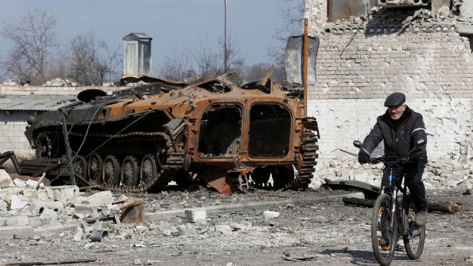 Un residente pasa en bicicleta junto a un vehículo blindado carbonizado durante la guerra entre Ucrania y Rusia.