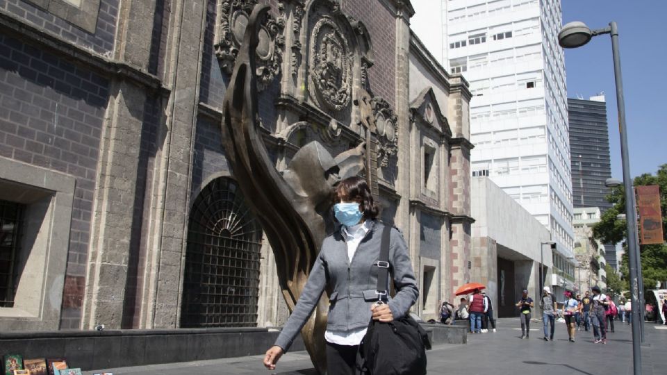 Una mujer pasea camina por calles de la ciudad usando un tapabocas.