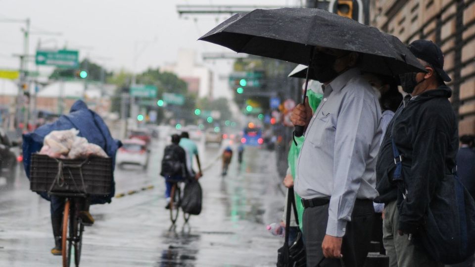 Una persona espera cruzar eje central mientras utiliza su paraguas para protegerse de la lluvia.