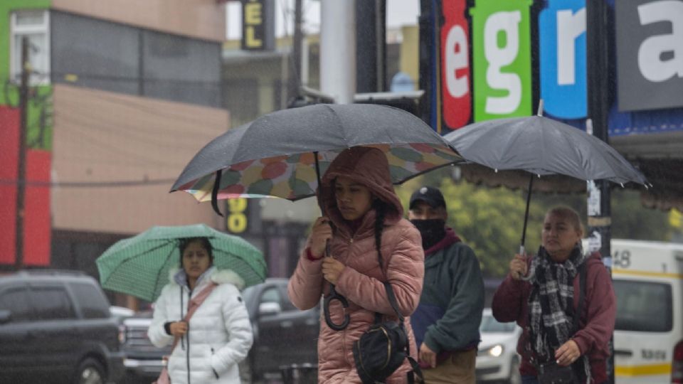 Personas cubriéndoselos de la lluvia con paraguas en la Zona Centro de Tijuana.

