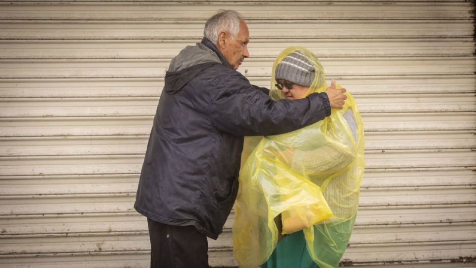 Hombre de la tercera edad cubriendo a mujer con impermiable tras las lluvia.