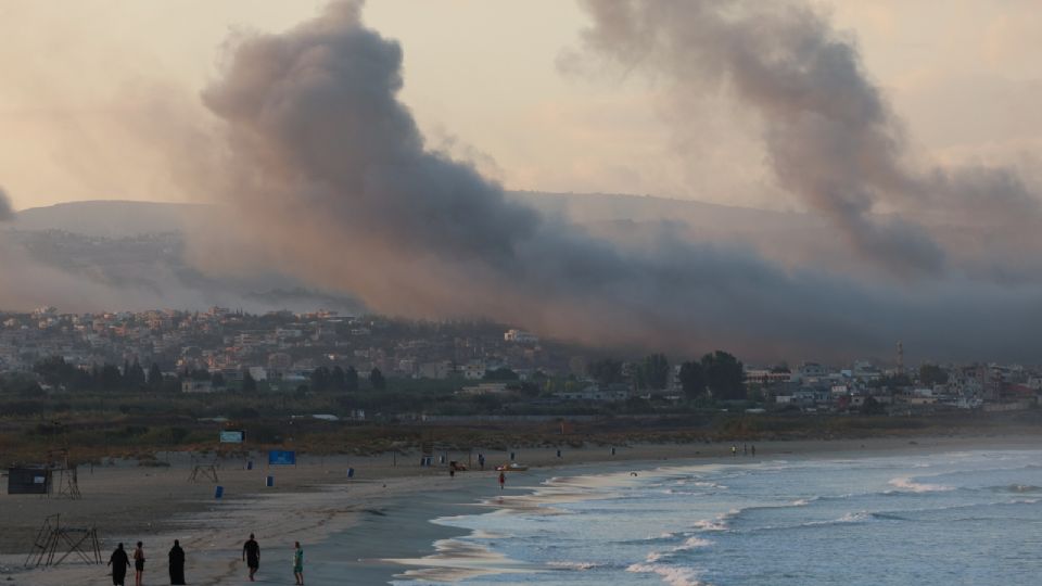 Un grupo de personas camina por una playa mientras el humo se cierne sobre el sur del Líbano tras los ataques israelíes, en medio de las hostilidades transfronterizas entre Hezbolá y las fuerzas israelíes, visto desde Tiro, sur del Líbano, 23 de septiembre de 2024.