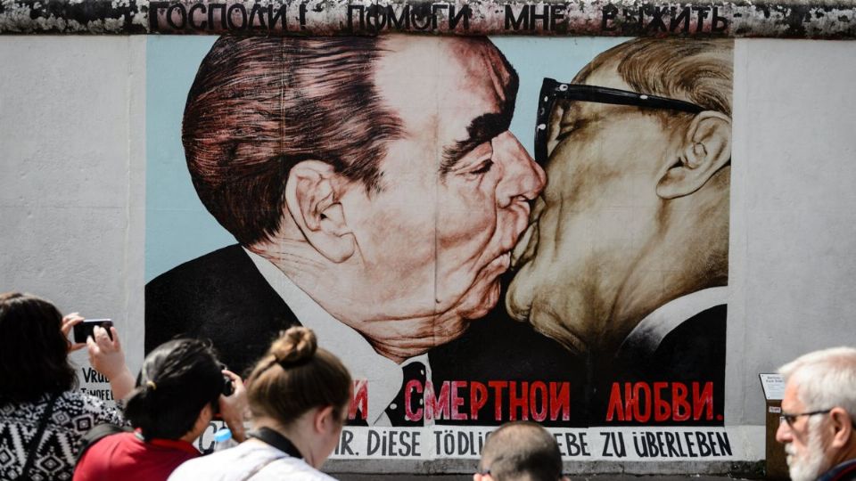 Turistas fotografían el mural 'Beso fraternal' del artista ruso Dmitri Vrúbel en el muro de Berlín.