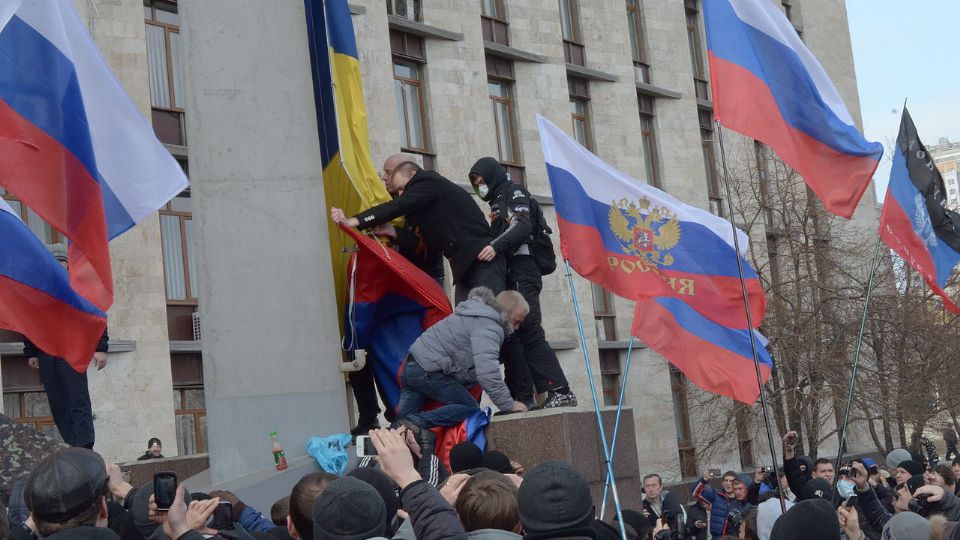 Manifestantes prorrusos retirando la bandera de Ucrania en un edificio en el óblast de Donetsk