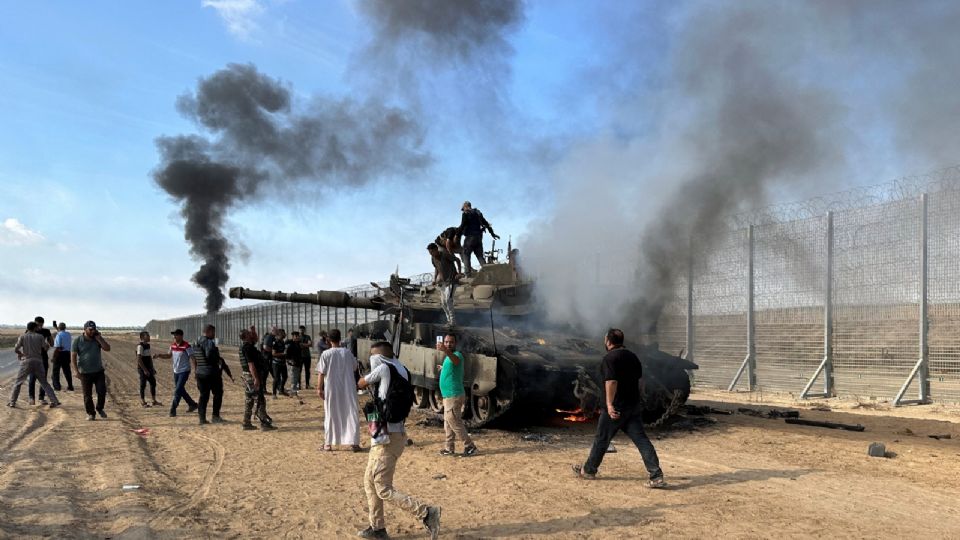 Palestinos reaccionan mientras un vehículo militar israelí arde tras ser alcanzado por atacantes que se infiltraron en zonas del sur de Israel.