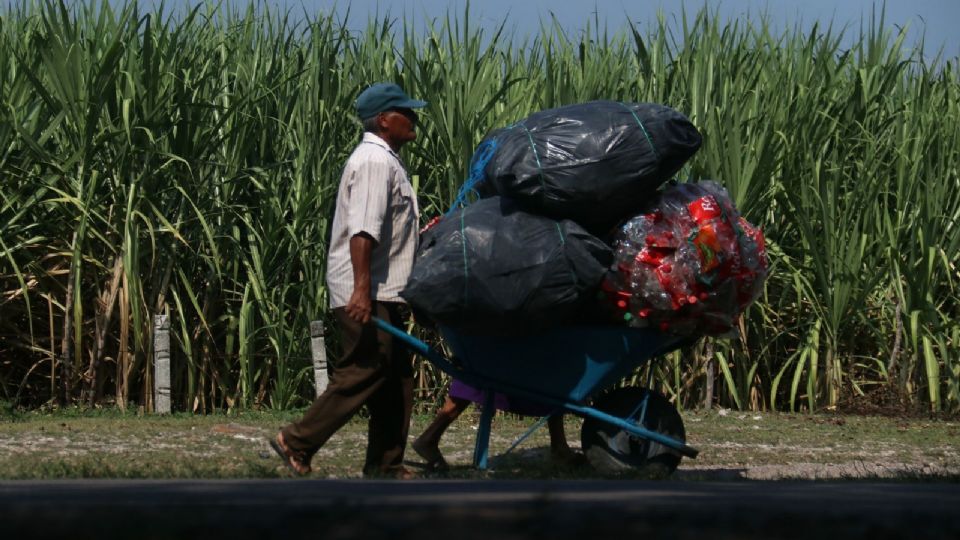 Un hombre de la tercera edad lleva en una carretilla bolsas de basura llenas de botellas de plástico que venderá para allegarse algunos pesos, su esposa lo acompaña.