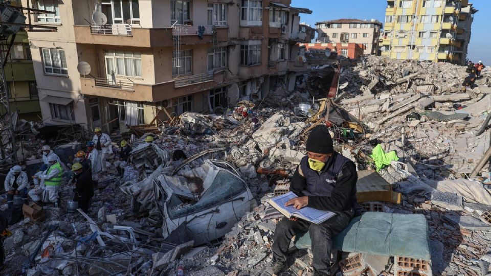 Un hombre lee el Koran mientras cuerpos de rescate trabajan en el lugar del colapso.