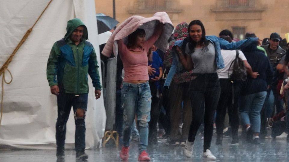 Capitalinos se cubrieron de las lluvias en el Zócalo capitalino.