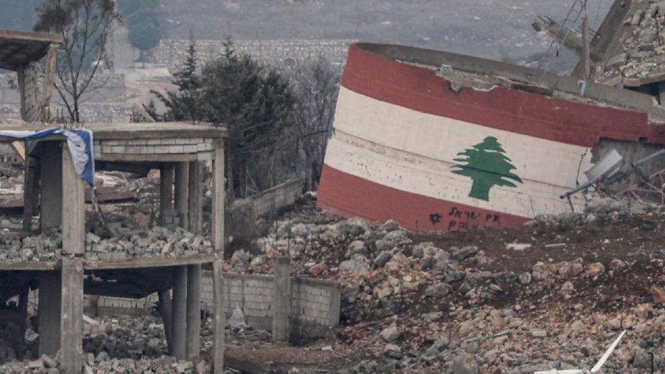 Una bandera israelí en un edificio destruido (izq.) cerca de un tanque de agua dañado pintado con la bandera libanesa (der.) en medio de los escombros de los edificios destruidos en la aldea de Meiss El-Jabal, tras el alto al fuego en Líbano.