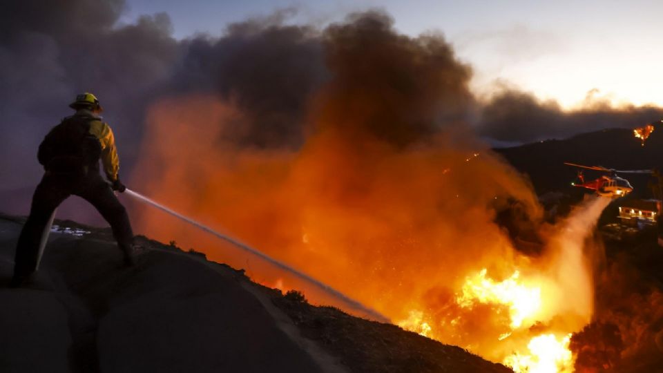 Los bomberos del condado de Los Ángeles usan mangueras y lanzan agua desde un helicóptero para combatir el incendio forestal de Palisades en Pacific Palisades, California.