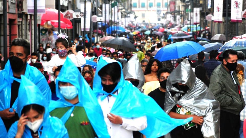 Decenas de personas caminan por la calle de Madero mientras se protegen de la lluvia con paraguas y plásticos.