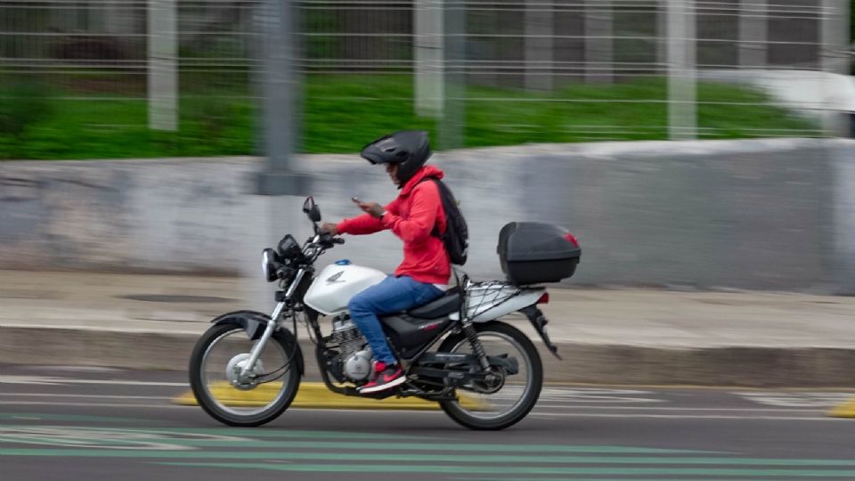 Un motociclista revisa el celular mientras conduce sobre Paseo de la Reforma.