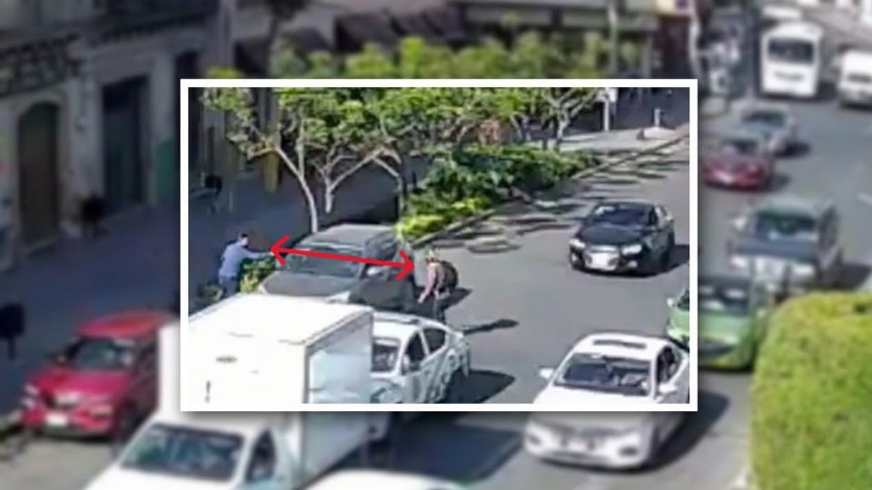 Toma elevada y ampliada de la escena donde se observa a un sujeto en la acera acercándose a un sedán gris.